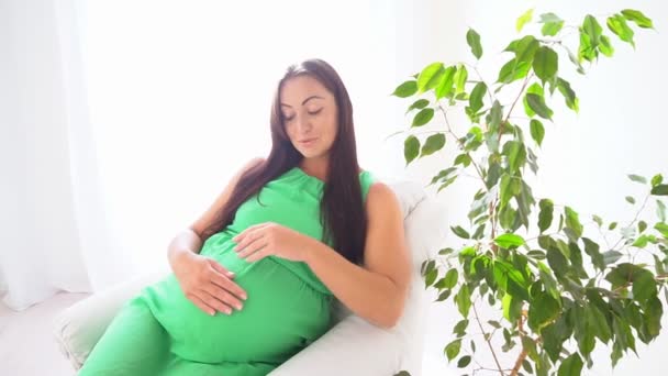 Una mujer embarazada está sentada en una habitación blanca — Vídeos de Stock