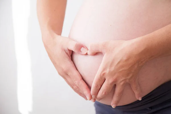 The stomach of a pregnant woman and hands happiness heart — Stock Photo, Image