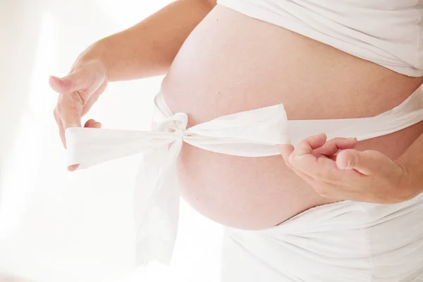 A pregnant womans belly and white bow gift — Stock Photo, Image