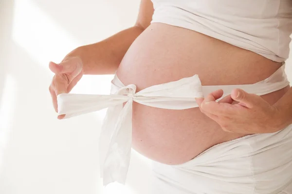 A pregnant womans belly and white bow gift — Stock Photo, Image