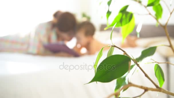 Мати і молодий син лежати на ліжку і користуються Інтернетом на планшеті — стокове відео