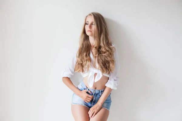 Chica en pantalones cortos azules rubia posando contra una pared —  Fotos de Stock