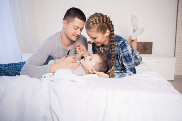 mom dad and son in the morning lying on the bed at home in a good mood