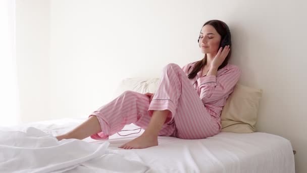 Kvinna som lyssnar på musik med stora hörlurar på sängen i — Stockvideo