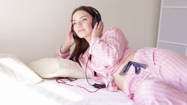 Vrouw in pyjama op de bed-dansen op muziek van hoofdtelefoons — Stockvideo