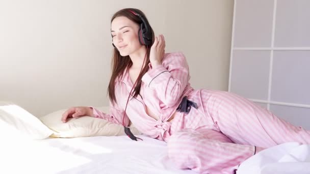 Женщина в пижаме на кровати утром, танцует под музыку из наушников — стоковое видео