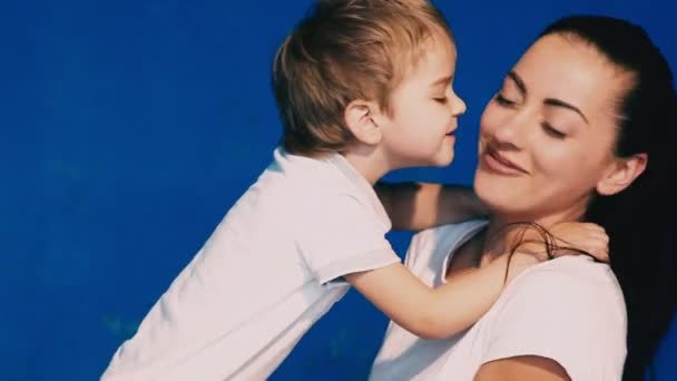 Moeder en zoon spelen lachen en kussen op een blauwe achtergrond — Stockvideo