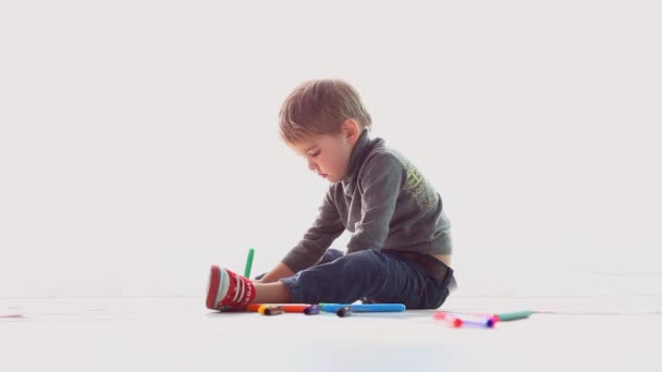 Menino desenha lápis coloridos em papel em uma sala branca — Vídeo de Stock