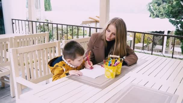 Мама і молодий хлопчик малюють олівцями за столом — стокове відео