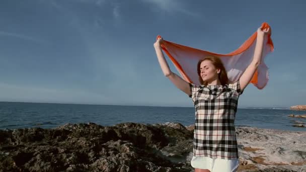 Gyönyörű nő a tengerparton, közel a tenger, a szél egy kendő — Stock videók