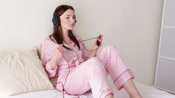 Woman listening to music with big headphones on the bed in — Stock Video