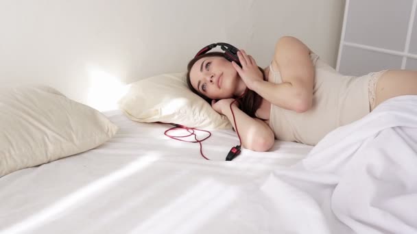 Frau in Dessous liegt im Schlafzimmer und hört Musik aus großem Kopfhörer — Stockvideo