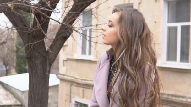 Chica en abrigo posando detrás de la valla en la calle — Vídeos de Stock