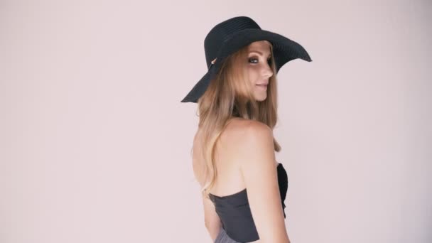 Hermosa chica en un sombrero con un ala grande posando sobre un fondo blanco — Vídeo de stock