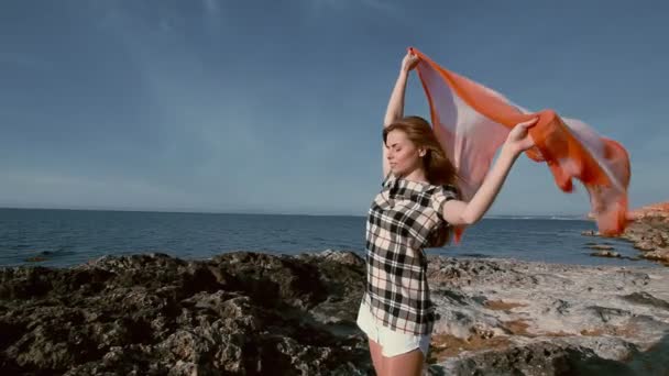 Vacker kvinna på stranden nära havet med en halsduk i vinden — Stockvideo