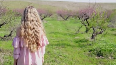 pembe elbiseli sarışın kız yemyeşil bahçede yürür
