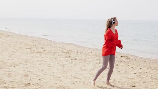 A mulher ouve música em grandes fones de ouvido na praia junto ao mar — Vídeo de Stock