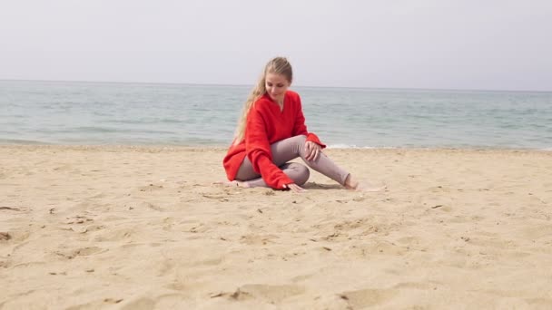 Blonde fille est assis sur le sable par la mer et posant pour une séance photo — Video