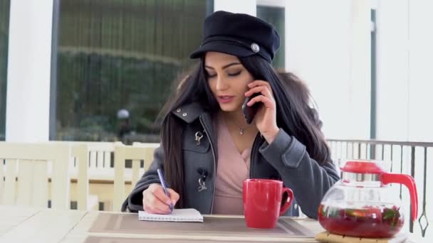 Uma mulher em um restaurante falando ao telefone e bebendo chá — Vídeo de Stock