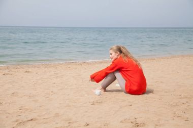 sarışın kumlu bir plaj üzerinde oturur ve denize bakarak