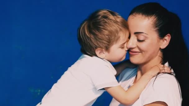 Madre e hijo jugar risa y beso en un fondo azul — Vídeo de stock