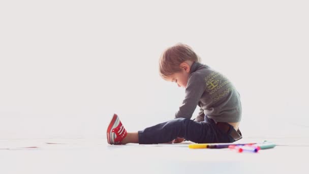 Μικρό αγόρι εφιστά χρωματιστά μολύβια σε χαρτί σε ένα λευκό δωμάτιο — Αρχείο Βίντεο