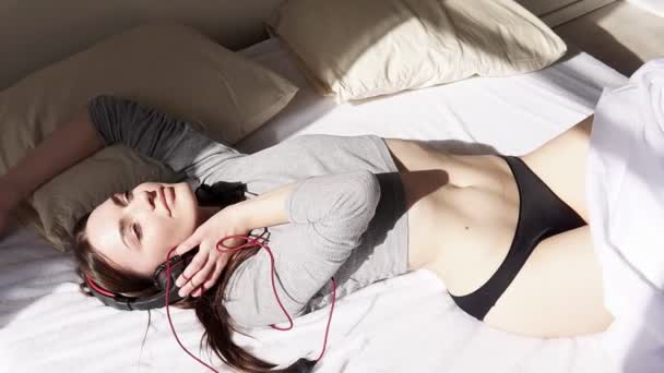 Woman in lingerie in bedroom listening to music with big headphones — Stock Video