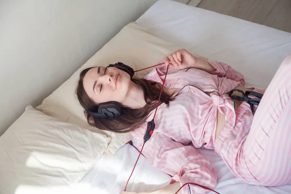 Brunette vrouw in roze pyjama's, luisteren naar muziek met koptelefoon — Stockfoto