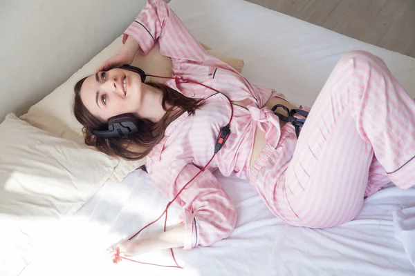 ヘッドフォンで音楽を聴くピンクのパジャマでブルネットの女性 — ストック写真