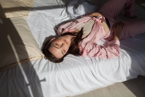 Брюнетка в розовом пижаме лежит на кровати — стоковое фото