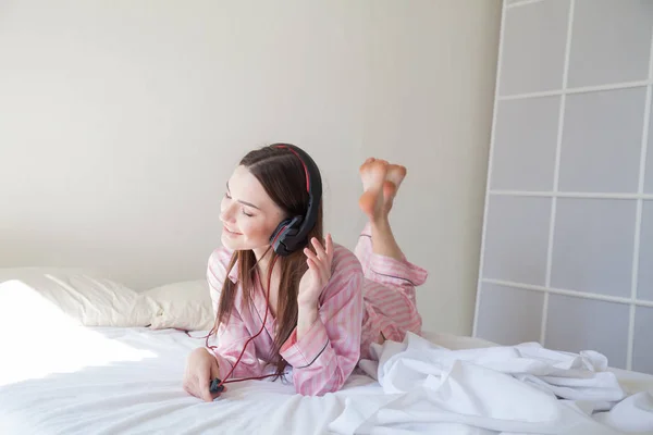 Bruneta žena v růžové pyžamo poslechu hudby se sluchátky — Stock fotografie