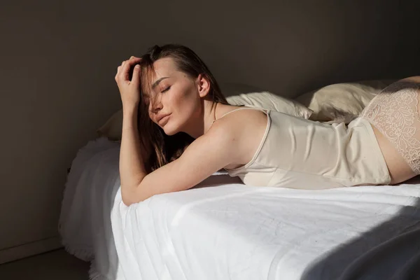 Morena mujer en ropa interior gris se encuentra en la cama en el dormitorio —  Fotos de Stock