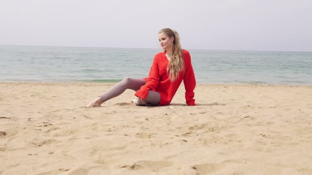 Blond flicka sitter i sanden vid havet och poserar för ett foto shoot — Stockvideo