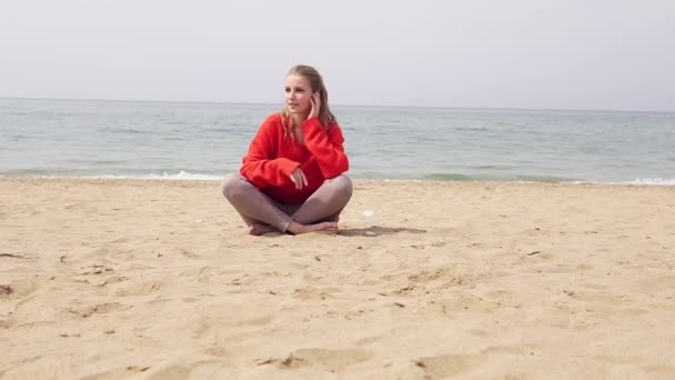 Blonde zit op een zandstrand in de buurt van de zee — Stockvideo