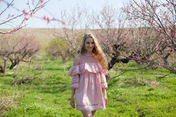 Блондинка гуляет по саду цветущим персиком — стоковое фото