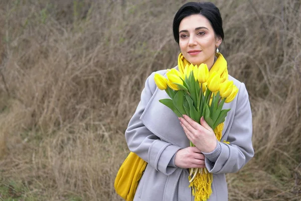 Brünette Frau in Mänteln mit gelben Tulpen — Stockfoto