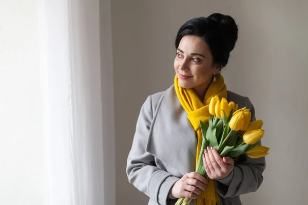 Mulher morena em casacos com tulipas amarelas — Fotografia de Stock