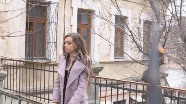 Chica en abrigo posando detrás de la valla en la calle — Vídeos de Stock