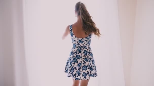 Chica en un vestido con flores se para en la ventana — Vídeos de Stock