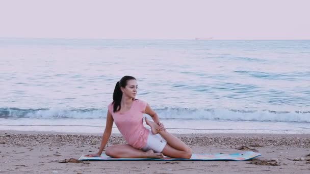A menina está envolvida em ginástica, ioga na praia da costa do mar — Vídeo de Stock