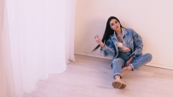 Μελαχρινή κοπέλα σε τζιν κοστούμι κάθεται στο πάτωμα — Αρχείο Βίντεο