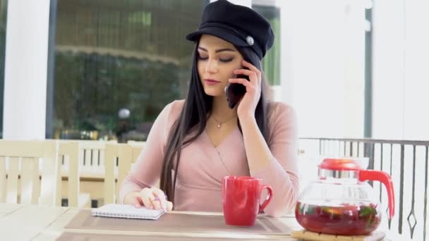Женщина в ресторане разговаривает по телефону и пьет чай — стоковое видео