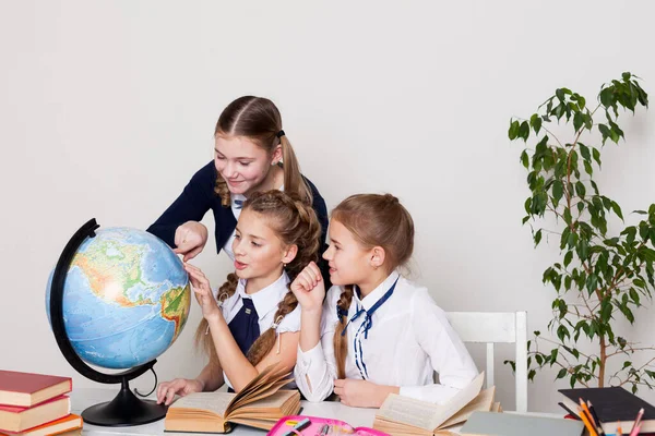 Três alunas na mesa estudam o globo em uma aula de geografia — Fotografia de Stock