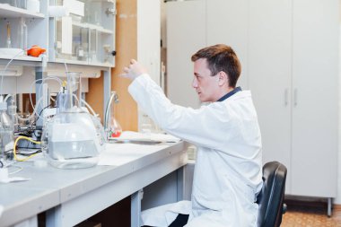 Erkek genç bilim adamı laboratuvarda sıvılarla kimyasal deneyler yapıyor.