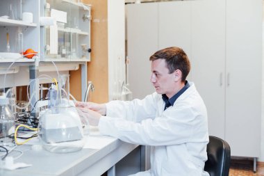 Erkek genç bilim adamı laboratuvarda sıvılarla kimyasal deneyler yapıyor.