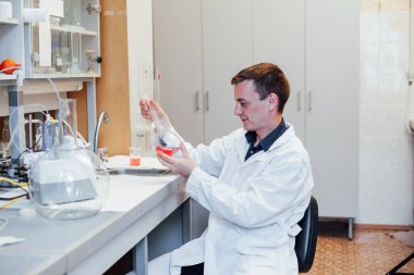 Erkek genç bilim adamı laboratuvarda sıvılarla kimyasal deneyler yapıyor.