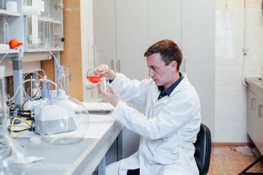 Erkek bilim adamı tıbbi laboratuvarda sıvılarla kimyasal deneyler yapıyor.