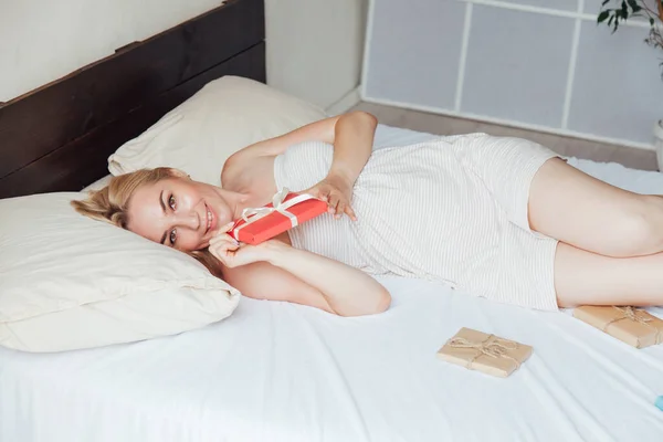 Mooie blonde vrouw opent geschenk in de ochtend in de slaapkamer op het bed — Stockfoto