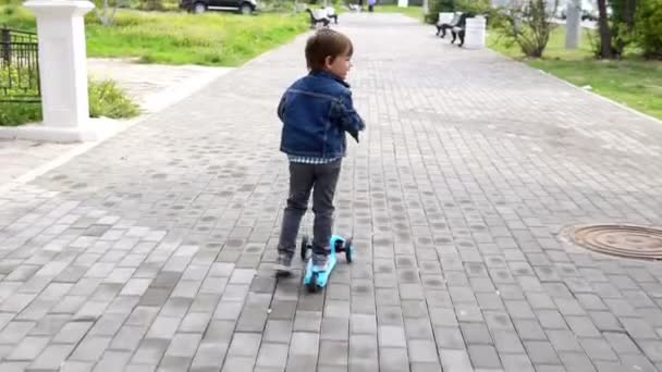 Liten pojke som rider på en skoter på gatan — Stockvideo