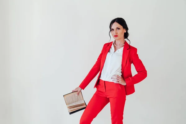 Portrait of a beautiful brunette woman with a book in a red business suit in the office — ストック写真